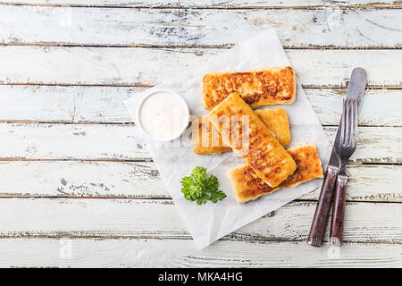 Crumbed golden fried fish fingers served with tartar sauce and salad on a white rustic wooden background, top view Stock Photo