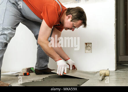 Laying Ceramic Tiles. Worker placing ceramic floor tile in position over adhesive. Stock Photo