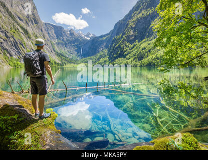 Young hiker standing at the shores of scenic Lake Obersee on a beautiful sunny day with blue sky in summer, Berchtesgadener Land, Bavaria, Germany Stock Photo