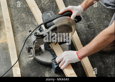 Worker cuts wood bars using a circular saw. Stock Photo