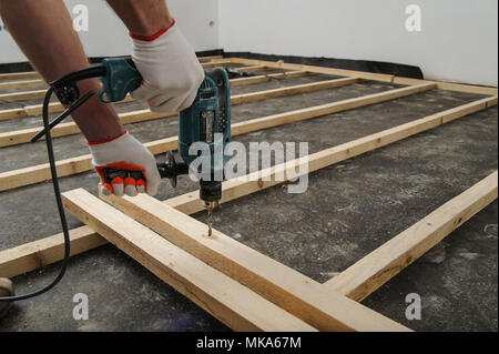 Worker drill holes in the wooden beams using an electric drill. Stock Photo