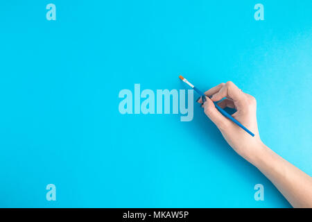 Hand holding paintbrush against blue background with vignette Stock ...