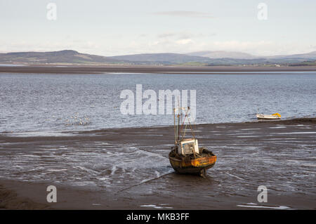 A fishing boat stands grounded on mudflats at low tide in Morecambe Bay in northern England. Stock Photo