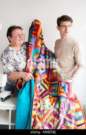 occupation, small business, happiness concept. there is a couple of coworkers of atelier, young designer and old seamstress, both are wearing eyeglass Stock Photo