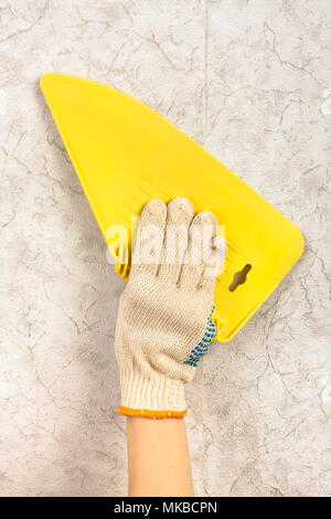 hand with spatula smoothing wallpaper on the wall during repair Stock Photo