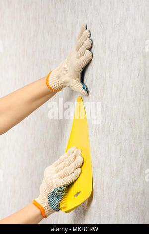 hands in gloves smoothing wallpaper with spatula on the wall during repair Stock Photo