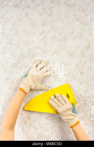 Hands in gloves smoothing wallpaper with spatula on the wall during repair. There is a place for your text in the top of picture. Stock Photo