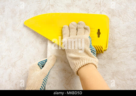 hands in gloves smoothing wallpaper with spatula on the wall Stock Photo