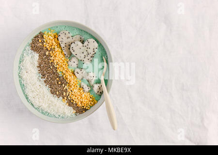 Tasty appetizing smoothie bowl with yogurt, coconut flakes, chia seeds, dragon fruit pieces and spirulina on textile background. Top View Stock Photo