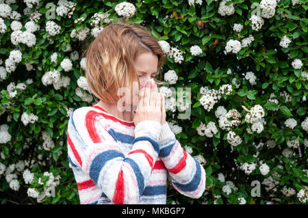Young woman blowing nose in front of blooming tree. Spring allergy concept Stock Photo