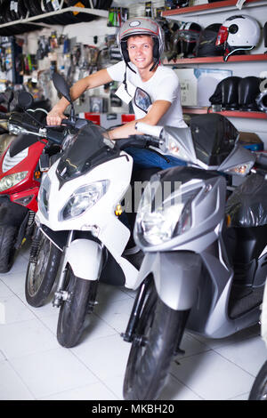 cheerful man sitting on the motorbike in the shop with helmet Stock Photo