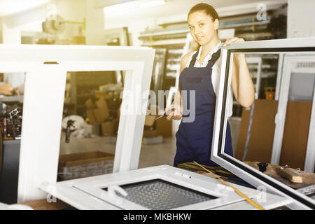 Diligent  positive  workwoman assembling PVC window in workshop with manual tools Stock Photo