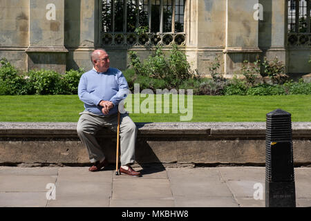 Obese man in a blue jumper sitting on the wall outside Kingâ€™s College Cambridge. Stock Photo