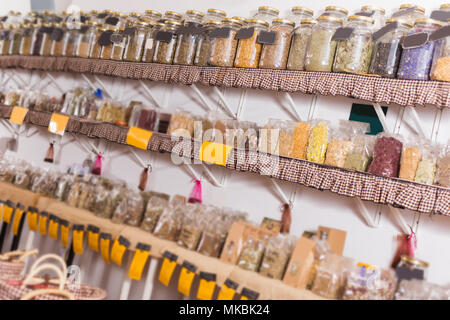 Big choice of glass cans with many different dried spices plants is standing on shelf in eco market. Stock Photo