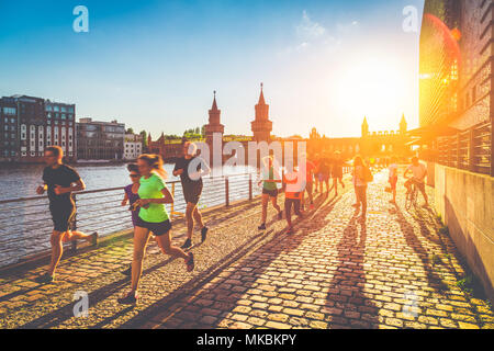 Group of female and male young runners jogging outside in golden evening light at sunset in summer with retro vintage filter effect Stock Photo