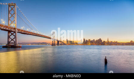 Classic panoramic view of San Francisco skyline with famous Oakland Bay Bridge illuminated in beautiful golden evening light at sunset in summer