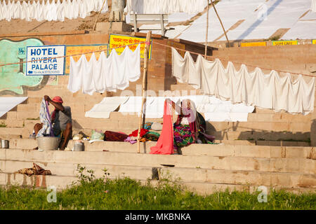 On the banks of the Ganges at Varanasi a gentleman does his washing in an old tub whilst a woman folds it neatly up. Stock Photo