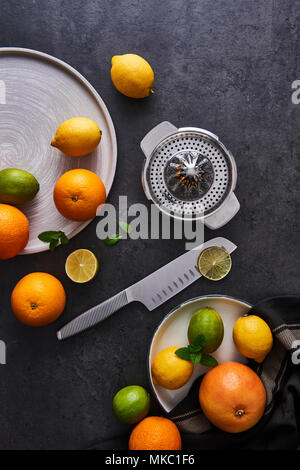 Top view of fresh ripe citruses. Lemons, limes, oranges and grapefruits with knife and citrus squeezer on dark concrete background. Flat lay with copy Stock Photo