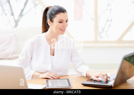 Beautiful young woman sitting at office desk behind computers and managing her business. Home office. Stock Photo