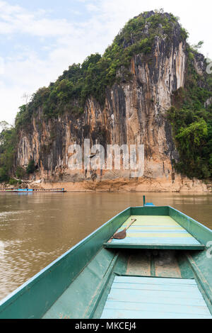 Boat on the Mekong River in front of a limestone cliff where the famous Pak Ou Caves are set. They are located near Luang Prabang in Laos. Stock Photo