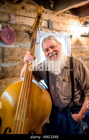 Portrait of a Silver Dollar City musician bass player smiling in Ozarks cabin with white beard, suspenders. Mountain music at Branson, Missouri, USA