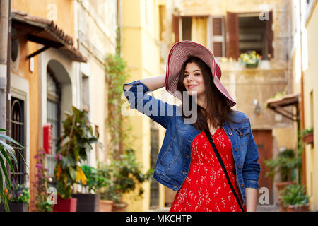 Cheerful pretty woman holding hat and posing at Trastevere in Rome, Italy. Stock Photo