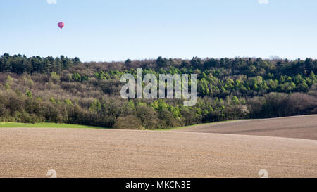 A hot air balloon floats over Wendover Woods and ploughed fields in the Hale in England's Chiltern Hills. Stock Photo