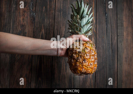 Female hand holding ripe pineapple on a wooden background. Stock Photo