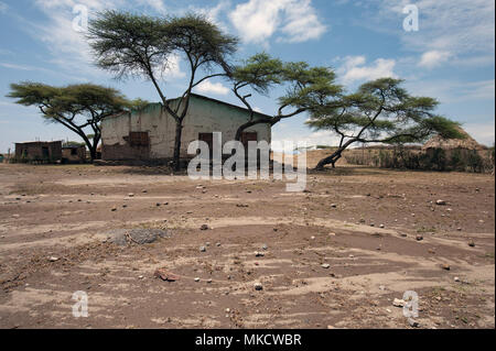 A small white one-storey peasant house among trees on red soil, South Ethiopia. Stock Photo