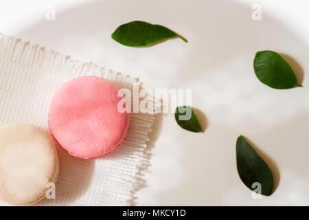 Pink, white Macaroons on light background, spring green petals, white napkin. Top view. Romantic morning, gift for beloved Stock Photo