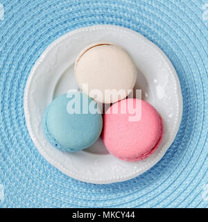 Three macaroons of different colors and different tastes in a white plate, top view. Square background Stock Photo