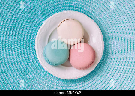 Three macaroons of different colors and different tastes in a white plate, top view. Romantic morning, gift for beloved. Breakfast on Valentin's, Mothers, Women's day Stock Photo