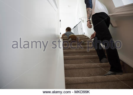 Father watching baby son crawling up stairs
