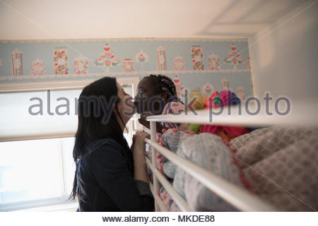 Affectionate mother kissing daughter waking in bunk bed