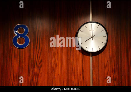 Number 88. Clock on wall showing eight o'clock next to number eight sign lucky eighty eight. Stock Photo