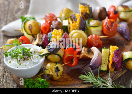 Grilled skewers with mixed vegetables served on a wooden cutting board with a vegan herb dip