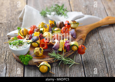 Grilled skewers with mixed vegetables served on a wooden cutting board with a vegan herb dip