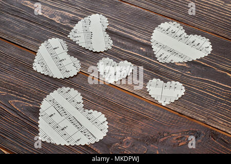 White paper hearts on dark wood. Decorative paper figures with musical notes on wooden background. Melody of love. Stock Photo