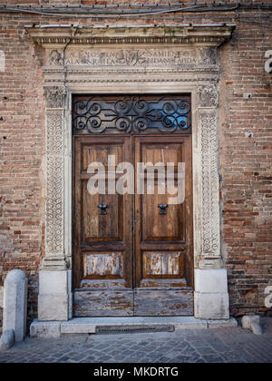 Old wooden portal with columns and architrave in white stone carved with floral motifs. Stock Photo