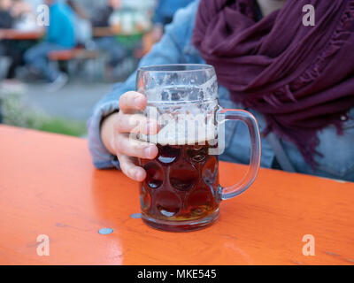 Woman gripping half empty beer mug mid drink Stock Photo