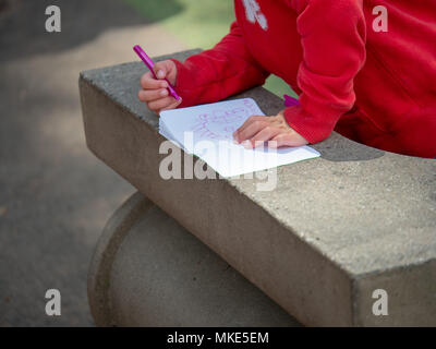 Child drawing pictures in paper notebook in a park outside Stock Photo