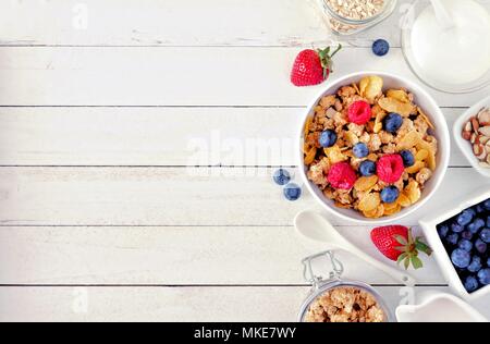 Cereal and ingredients for a healthy breakfast forming a side border over a white wood background. Top view. Copy space. Stock Photo