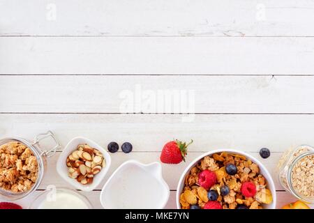 Cereal and ingredients for a healthy breakfast forming a bottom border over a white wood background. Top view. Copy space. Stock Photo