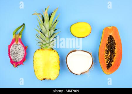Tropical fruit flat lay with pineapple, dragon fruit, papaya, mango, and coconut on a pastel blue background Stock Photo