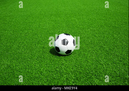 soccer ball classic black and white on green artificial grass, alone, football with much space for text and graphics around, for banner or invitation Stock Photo