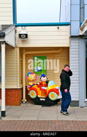 Man in casual dress walking past childrens' Noddy Car ride Stock Photo