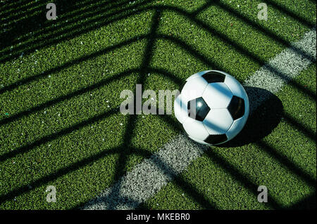 soccer ball classic black and white with shadows on the ground of an artificial football goal Stock Photo