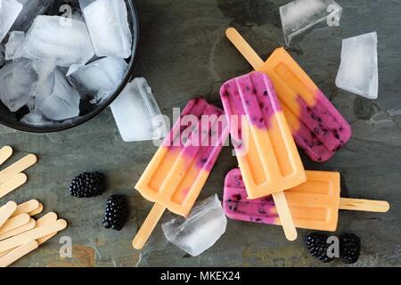 Mango blackberry ice pops in a cluster. Top view scene over a slate background. Stock Photo