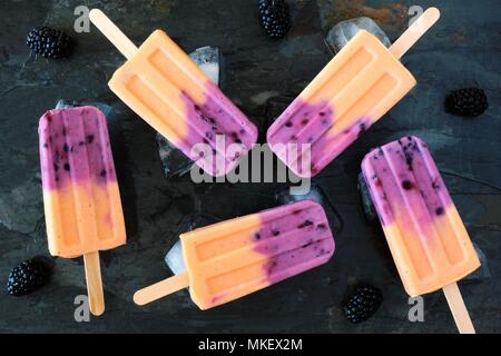Group of mango blackberry yogurt popsicles with ice. Top view on a dark background. Stock Photo