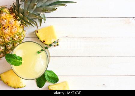 Glass of pineapple juice with fruit. Top view, side border on a white wood background. Stock Photo